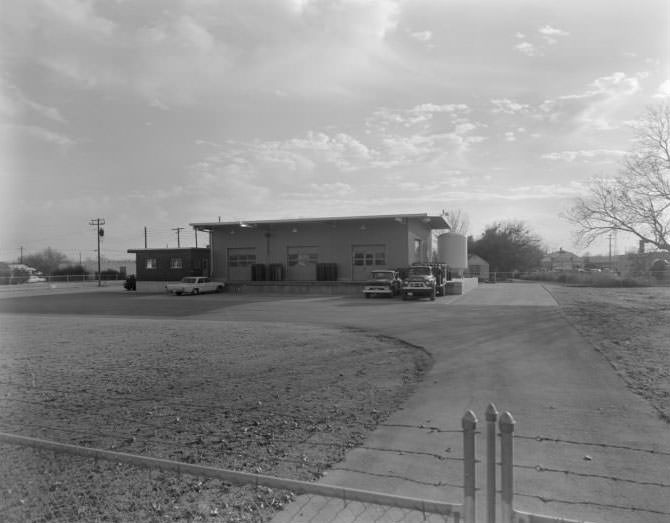 #159 Exterior view of building with loading dock. 2 trucks and 1 car parked in front of dock, 1962