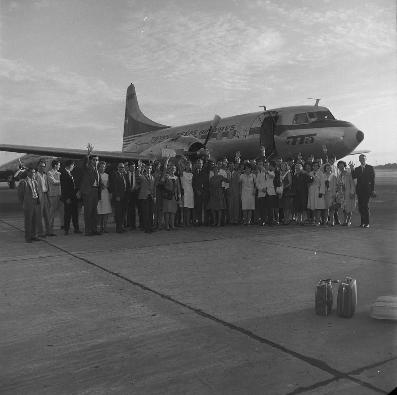 #165 Passengers and crew wave goodbye on the tarmac before departure at Mueller Airport. Plane is Convair 240. TTA DC-3 in left background, 1966