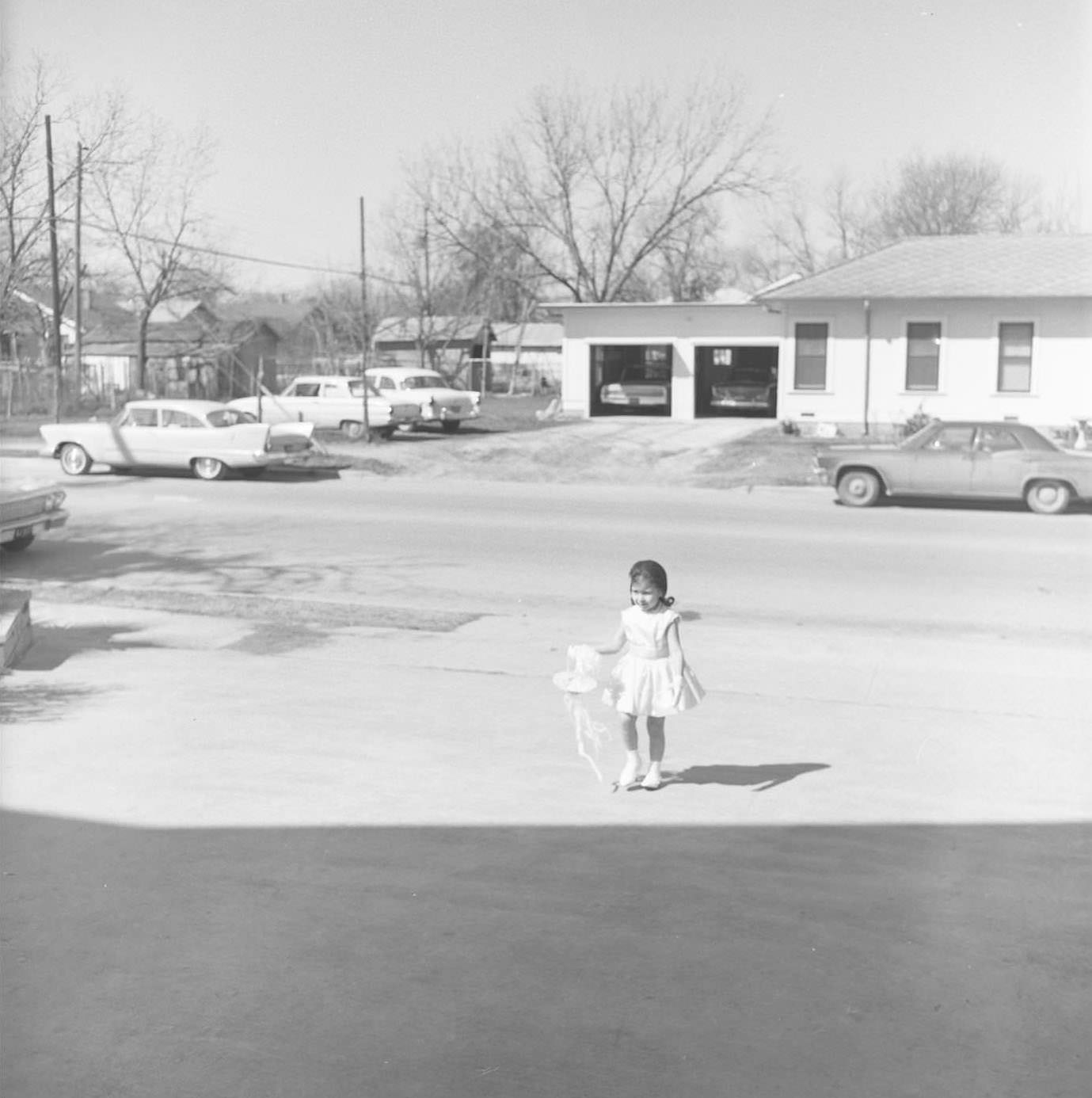 #168 Child of couple stands with bow in a driveway, 1965