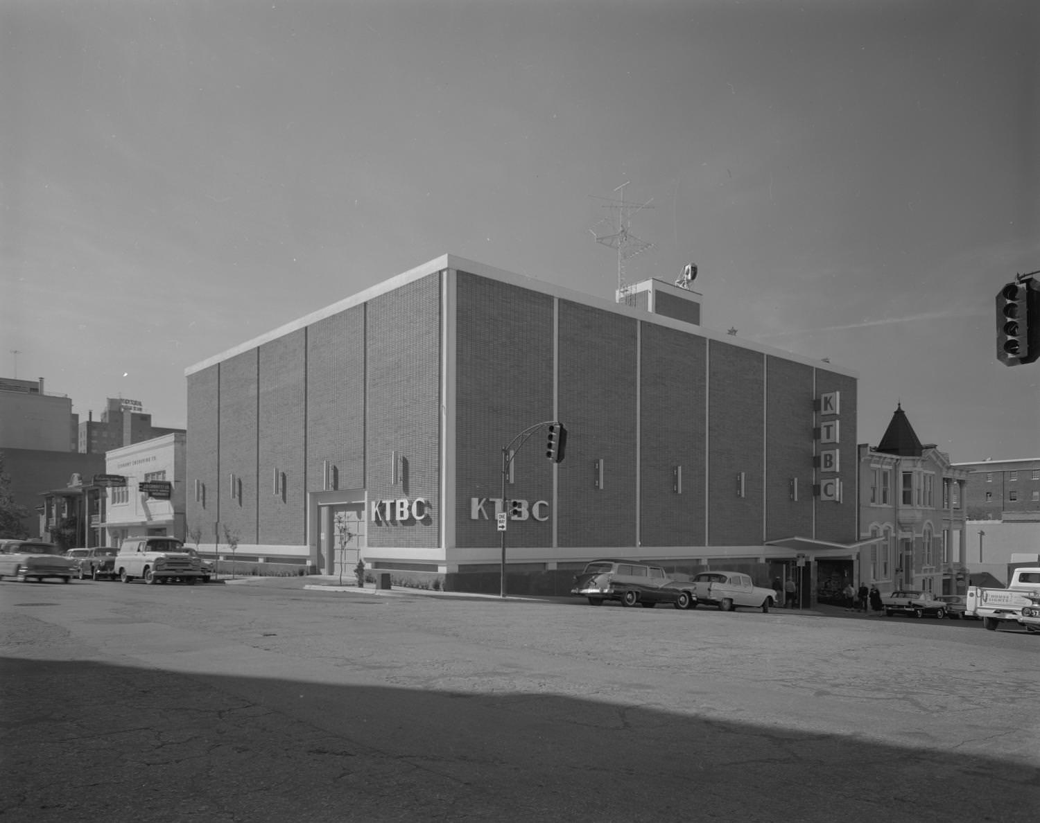 #69 KTBC Studio on a street corner with traffic lights for an intersection seen in the foreground, and cars seen both driving and parked on each street, Austin, 1960