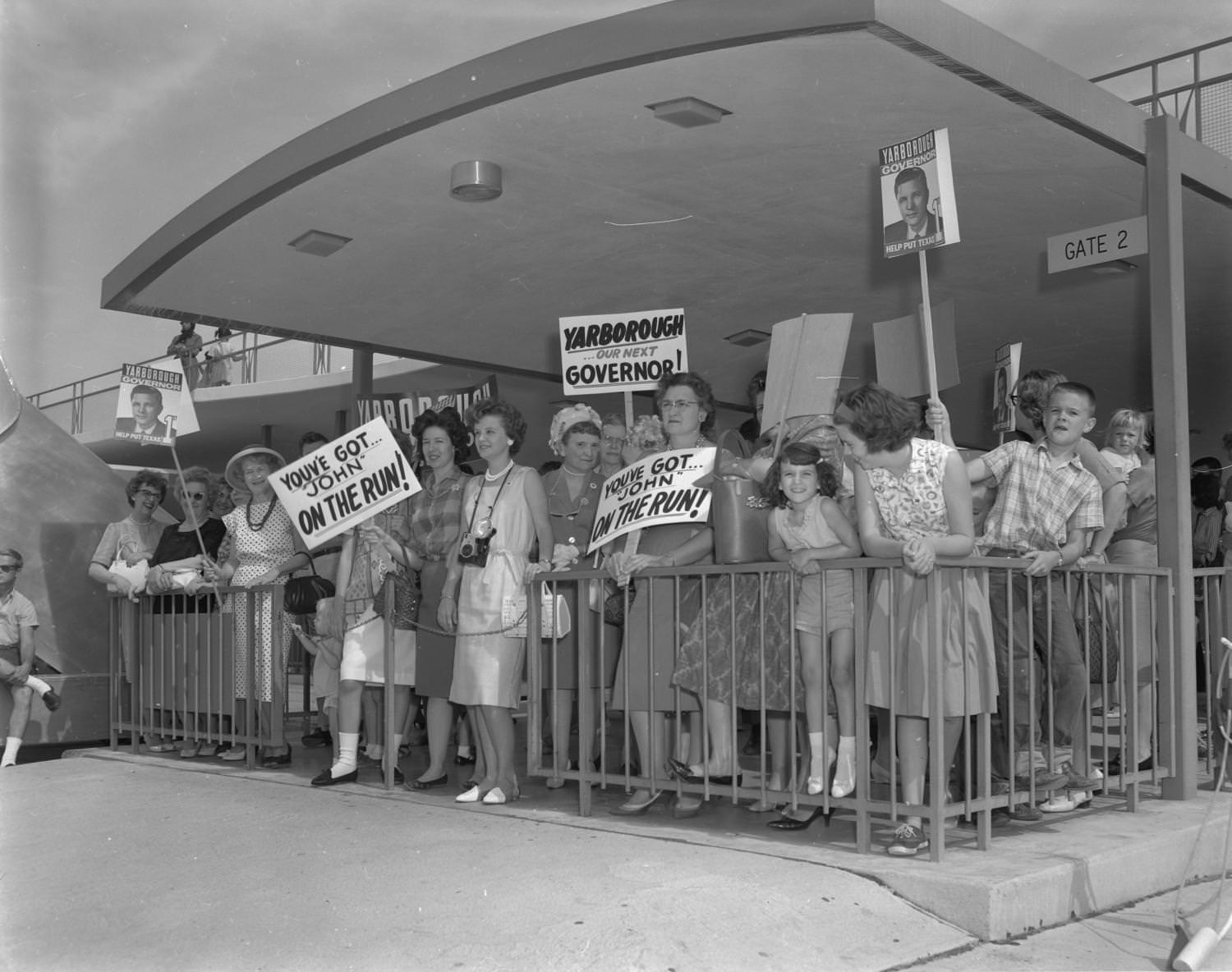 #196 Supporters of gubernatorial candidate, Don Yarborough, standing with signs in a fenced area, 1962