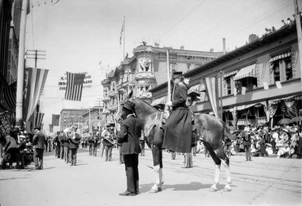 #59 An African American (Black) man stands near a woman on horseback, possibly a drum majorette, during a parade on 17th (Seventeenth) Street at California Street in downtown Denver, 1905