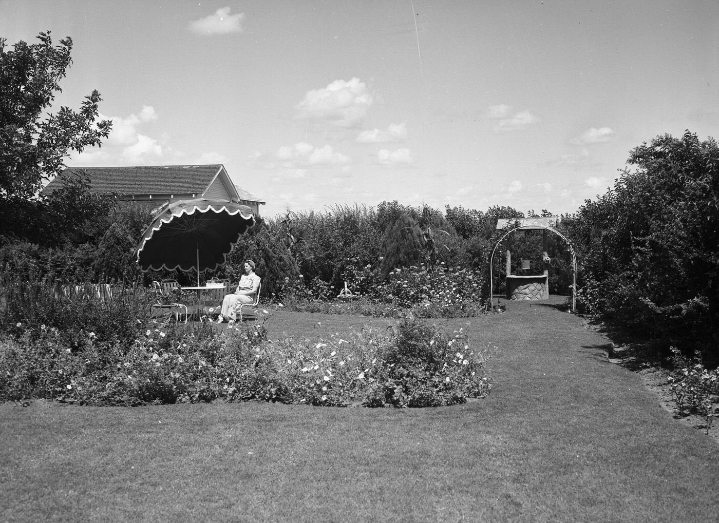 #9 Mrs. C. H. Bertram, shown sitting at an umbrella-protected table in her “outdoor living room,” which is surrounded with flowerbeds and hedges, 1940