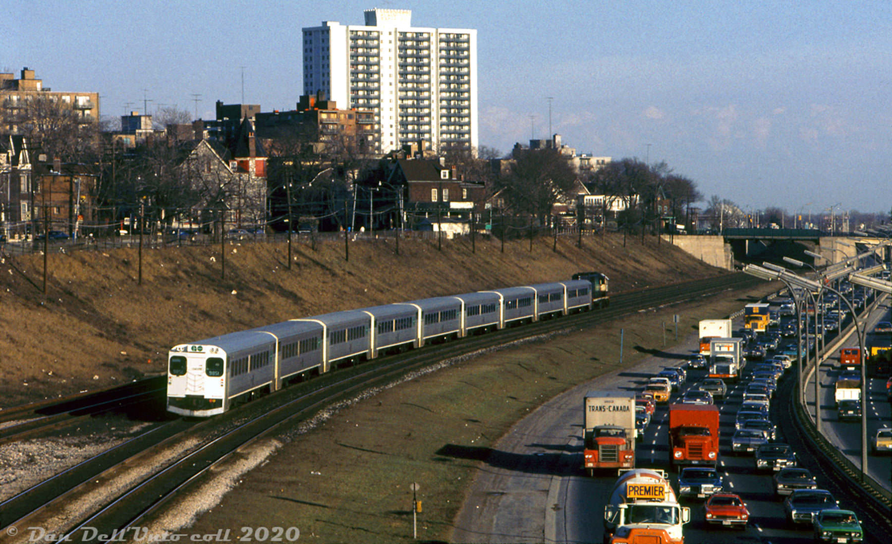 #133 A grungy March 1973 view along the Gardiner Expressway at Sunnyside, showing an inbound GO train heading to Union Station as PM rush hour traffic inches along the Gardiner out of the city.