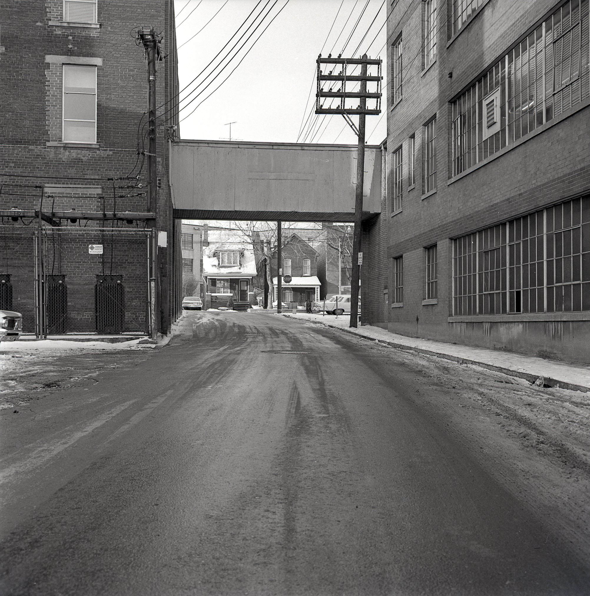 #94 Above-ground connection between two buildings at the west end of Pears Avenue, framing a view of a couple houses on Bedford Road, 1964