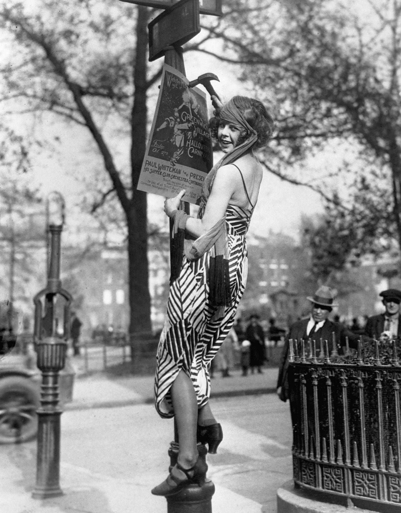 #40 A flapper hangs a poster to advertise the Greenwich Village Halloween Ball, at which Paul Whiteman is to perform.