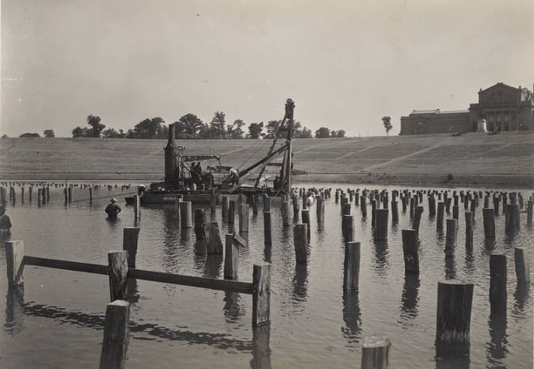 #78 Men using machinery to drive piers into the water of the Grand Basin, Forest Park, for construction of the stage for the Pageant and Masque of St. Louis, 1914