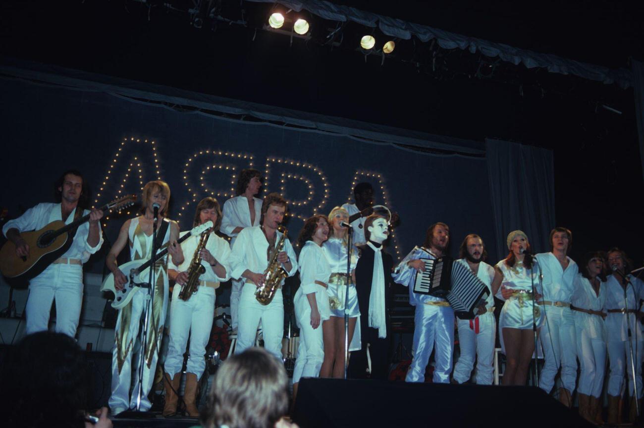 #19 Bjorn Ulvaeus, Agnetha Faltskog, Anni-Frid Lyngstad and Benny Andersson on stage with their backing band in 1977.