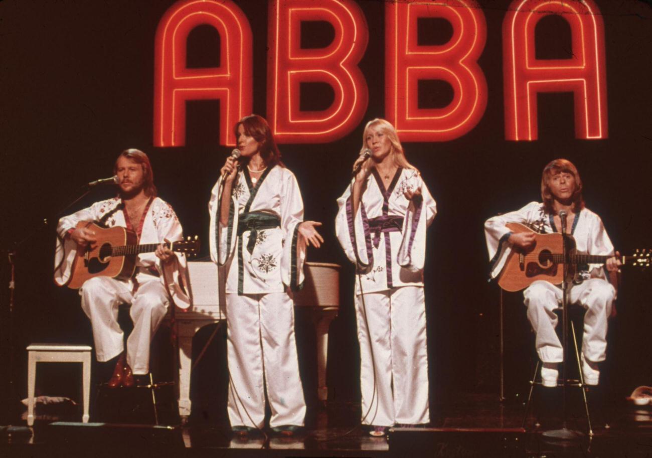 #32 Benny Andersson, Frida Lyngstad, Agnetha Faltskog, Bjorn Ulvaeus), wearing similar white Asian-influenced costumes, perform for the television program Midnight Special with a neon