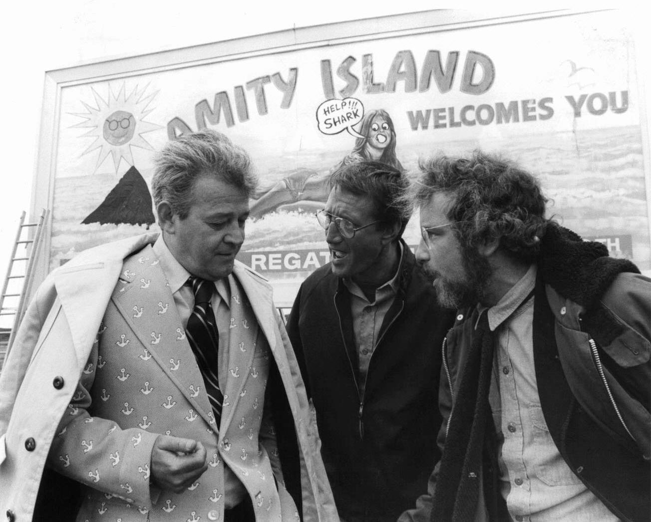 Murray Hamilton, Roy Scheider, and Richard Dreyfuss standing in front of defaced billboard in a scene from the film ‘Jaws’, 1975.