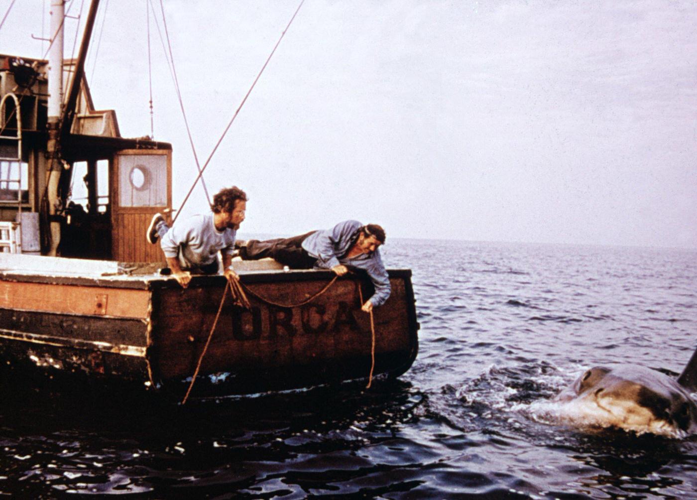 Richard Dreyfuss and Robert Shaw hold ropes while leaning off the back of their boat, ‘Orca,’ in pursuit of the giant Great White shark in a still from the film, ‘Jaws,’ 1975.