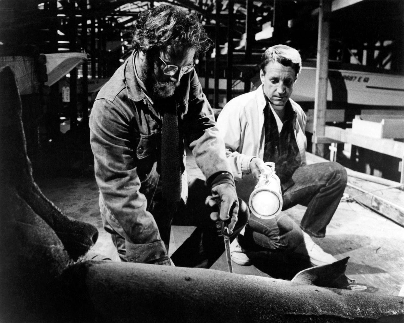 Police chief Martin Brody, played by Roy Scheider (1932 – 2008) holds a torch while marine biologist Matt Hooper (Richard Dreyfuss) cuts open the stomach of a recently caught tiger shark, in ‘Jaws’, 1975