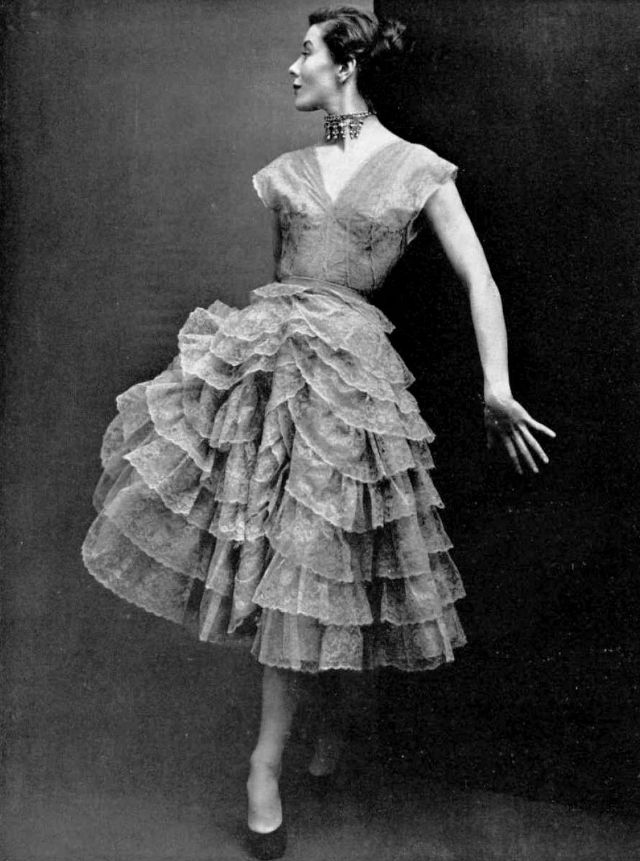 #74 Bettina in gray lace dress, skirt is wound round with frilly lace ruffles, by Robert Piguet, 1950