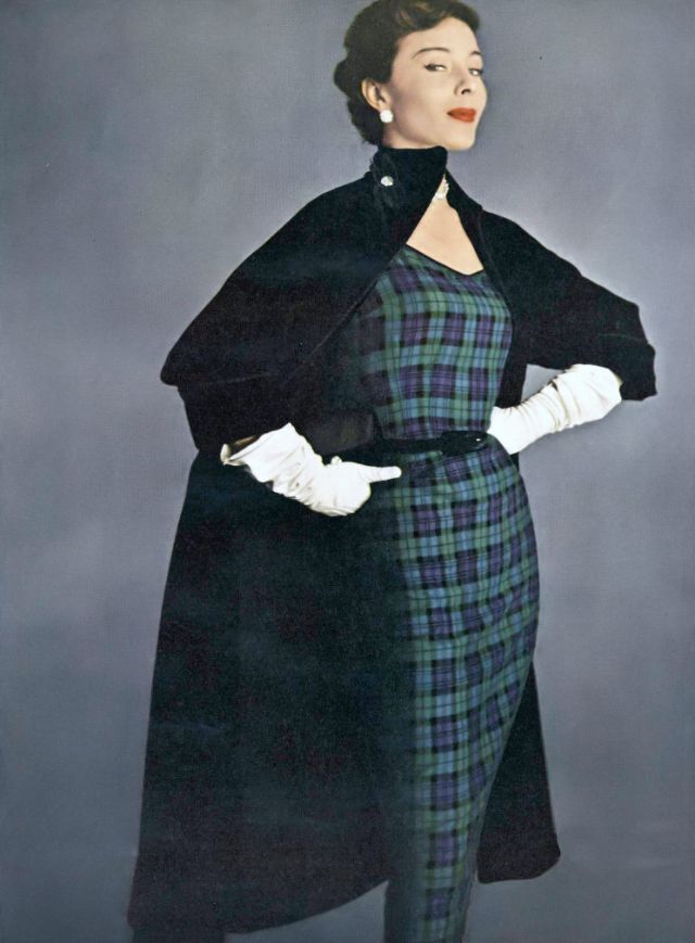 #75 Bettina in plaid wool worsted sheath under a big black velveteen coat inter-lined and braid-bound, both by H. & D., earrings by Kramer, Vogue, August 15, 1950