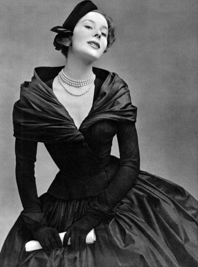#83 Bettina in dress of black matte wool bodice over black taffeta skirt and shawl, black cap with red rose completes the look by Christian Dior, 1951
