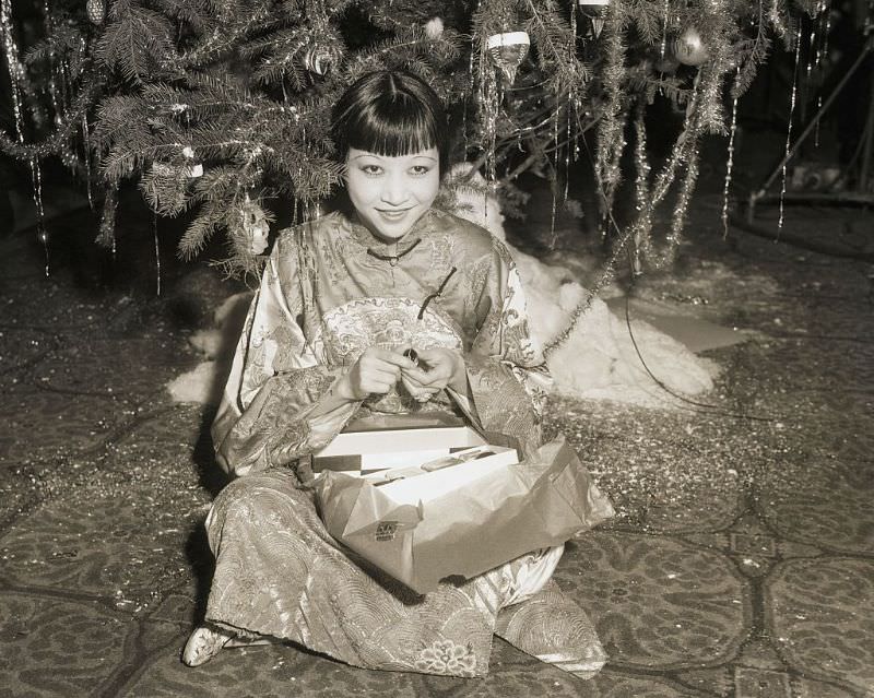 #83 Anna May Wong opens present under the tree at a Christmas celebration for Hollywood stars at the Christy Hotel in 1932.
