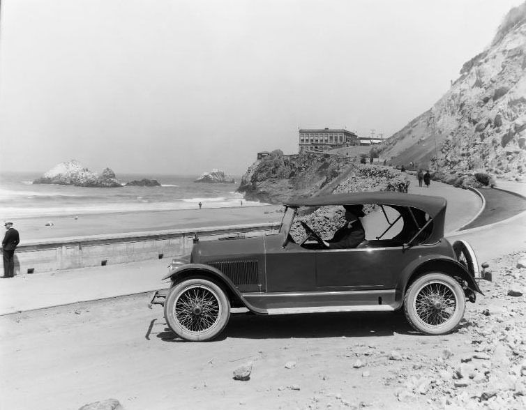 #25 Historic San Francisco Cliff House. Road and sidewalk construction has been completed on the curved road including new landscape work. A military man in uniform and Seal Rocks can be seen along the left, 1922