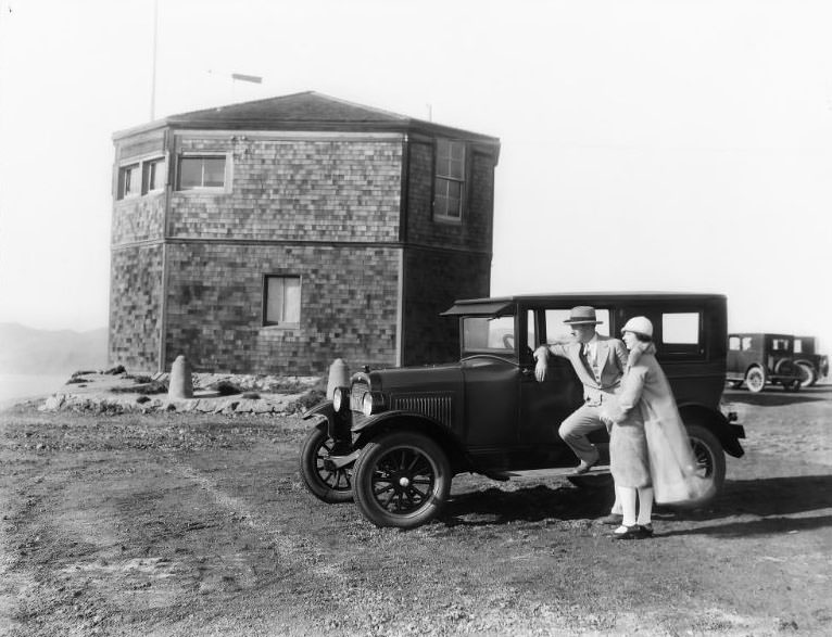 A 2-Door Sedan automobile pictured alongside the nearly completed historic “Octagon House” located at Lands End in San Francisco, California. Formally known as Point Lobos Marine Exchange Lookout Station, 1925