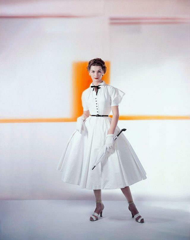 #4 Georgia Hamilton wearing a white matelassé cotton with puffed cupid sleeves below the dropped shoulder, a black bowtie, jet buttons and a patent belt, by Caroline Schnurer, Glamour, 1952