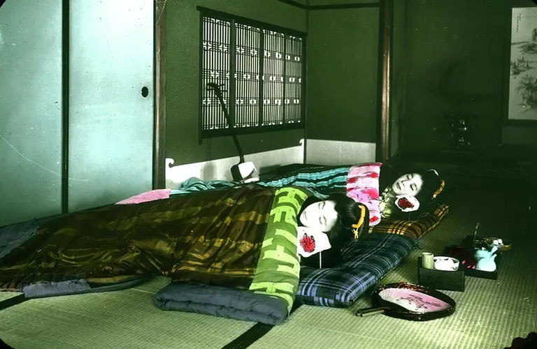 #2 Interior shot of two geishas asleep in bedding on floor mats; musical instrument, fan and implements for tea ceremony nearby.