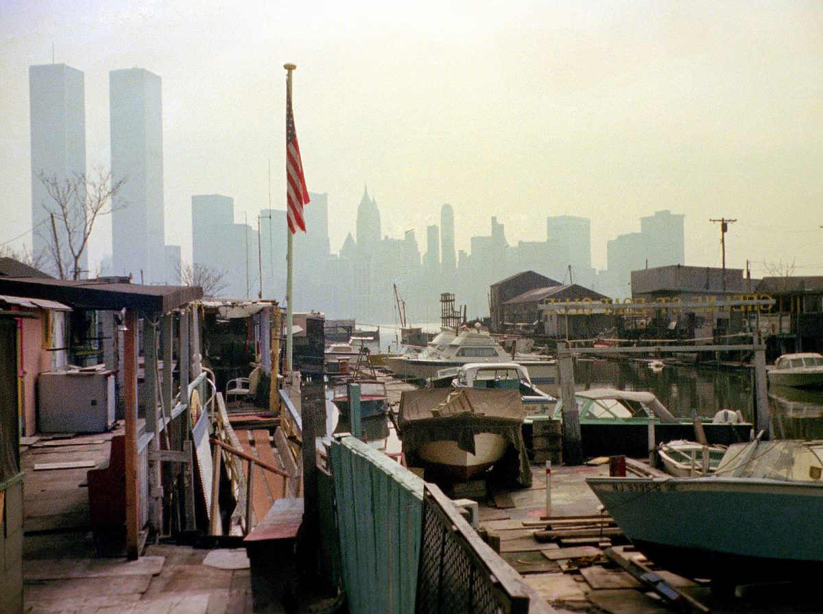 #17 The ramshackle Greene Street Boat Club in Jersey City with the Lower Manhattan skyline and the World Trade Center in the distance, March 1975