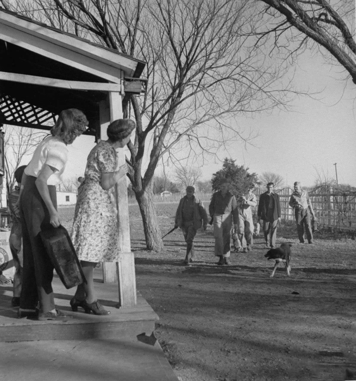#3 Mrs. James Ferdinand Irwin (L) standing on porch watching the men in her family, most recently returned fr. service in WWII, carrying home freshly shot rabbits and a cedar tree for Christmas family reunion.