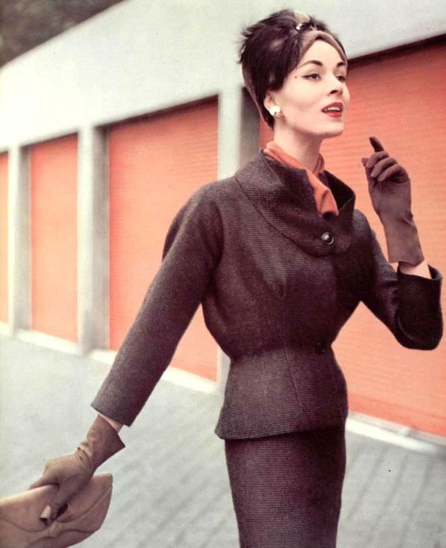 #19 Model in fine wool checked suit, jacket has expanded bust and flexible back, worn over jersey blouse, by Grès, hat by Legroux, clutch by Muth, 1956