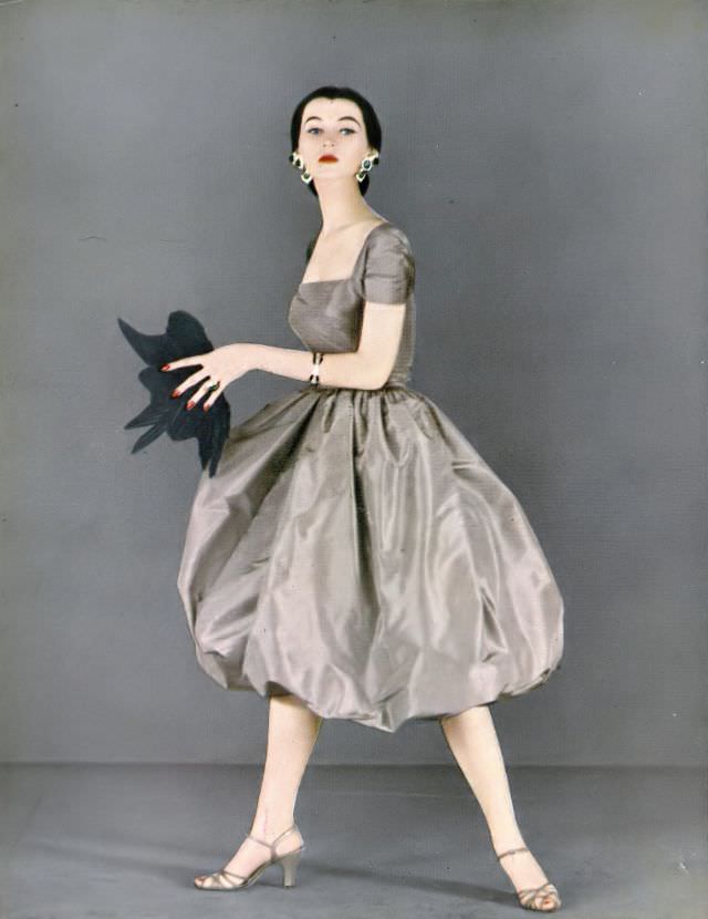 #1 Dovima in bouffant silk taffeta skirt with separate square-cut taffeta top by Mollie Parnis, Coro earrings, Hattie Carnegie fan, Harper’s Bazaar, February 1951
