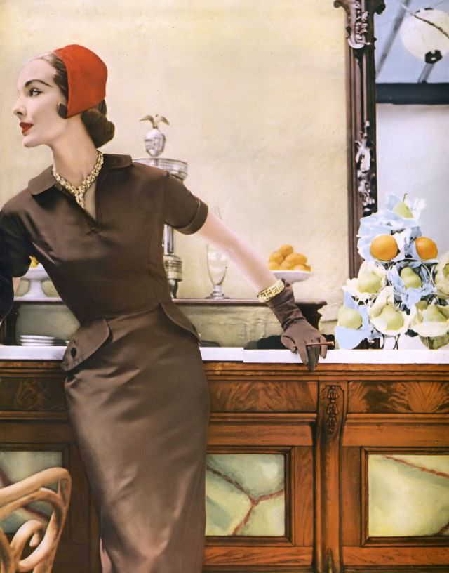 Cherry Nelms in taupe silk twill sheath by Mollie Parnis, red brushed velours cap by John Frederics, gold and diamond necklace and bracelet by Van Cleef &; Arpels, Vogue, July 1953