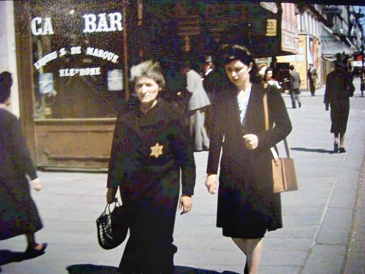 #15 An elderly woman walks along the street wearing the yellow star that Nazis forced Jews to wear.