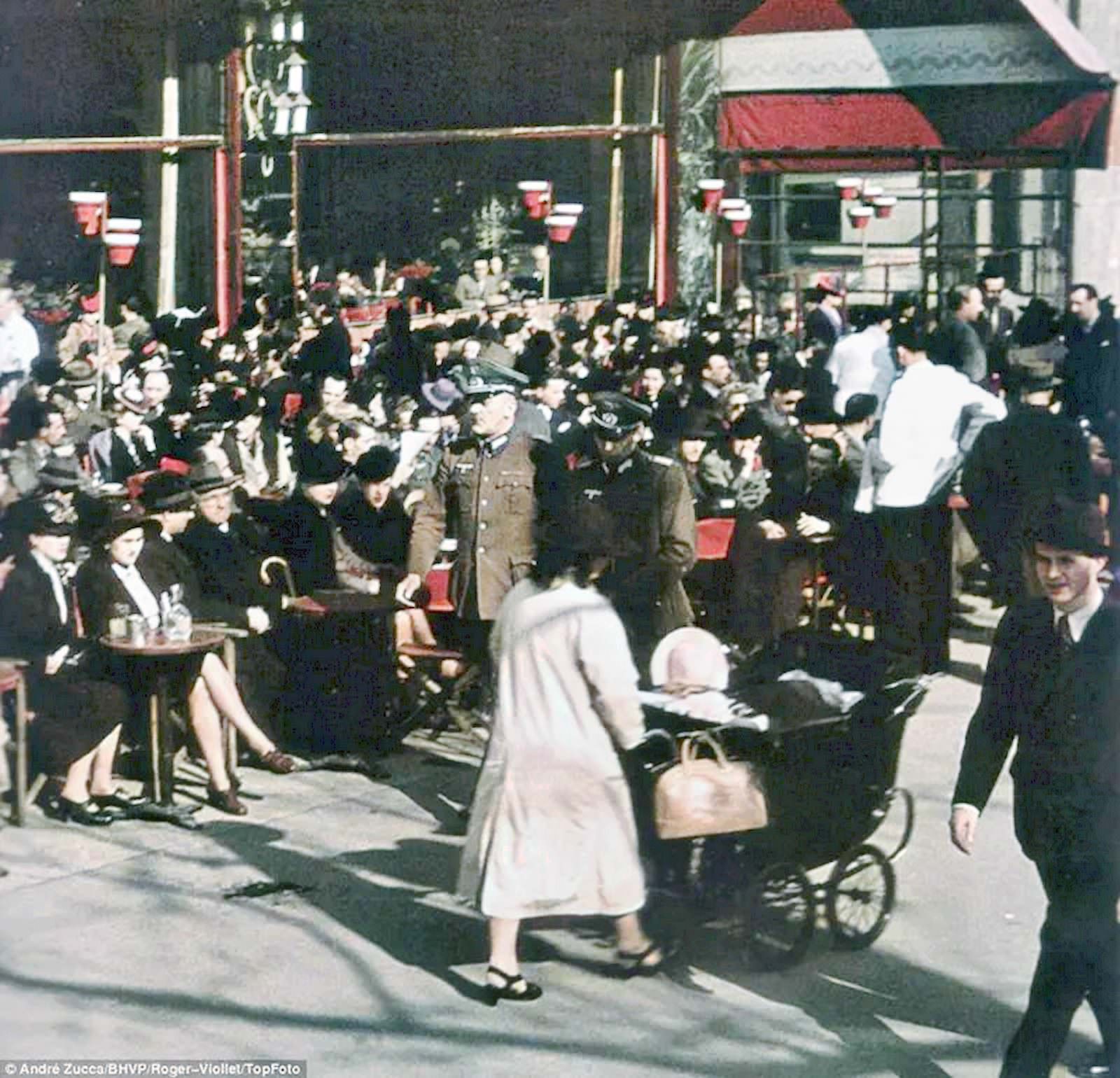 #64 Senior-looking German army officers stroll past a crowd of French enjoying the afternoon in one of Paris’s outdoor cafés.