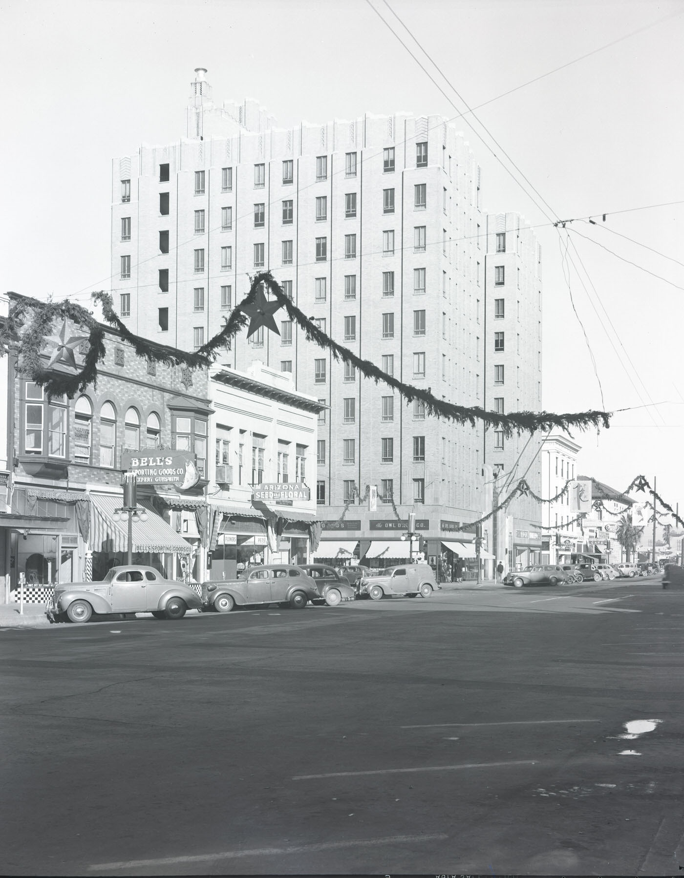 #75 1st Avenue. Depicts the 40 block of N. 1st Ave. Visible are Bell’s Sporting Goods (40 N. 1st), New Arizona Seed & Floral Co. (46 N. 1st), and Christmas decorations, 1941