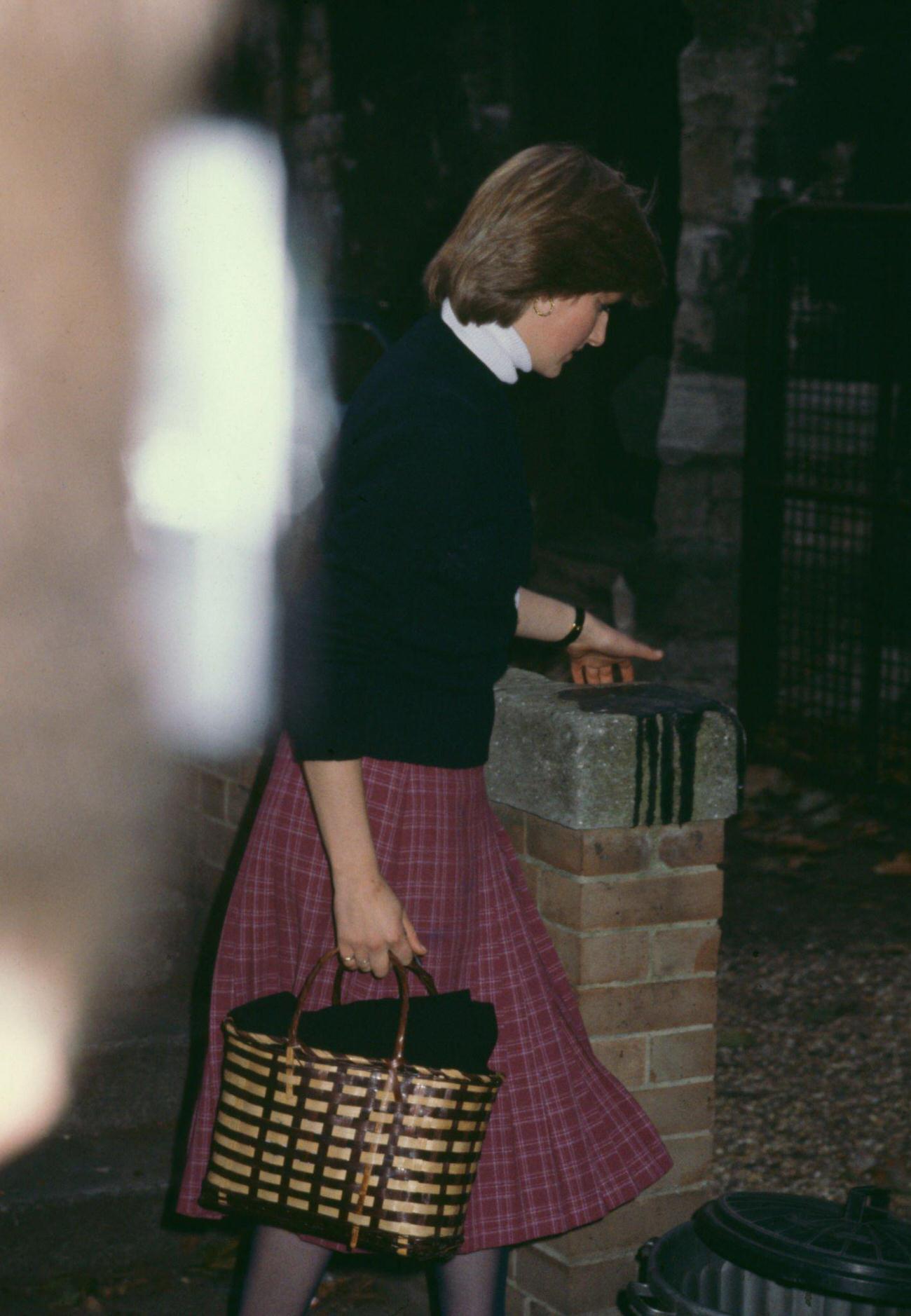 #11 Lady Diana wearing a dark sweater with a deep red plaid skirt, and carrying a brown handbag, leaves the Young England kindergarten in Pimlico, London, England, October 1980.