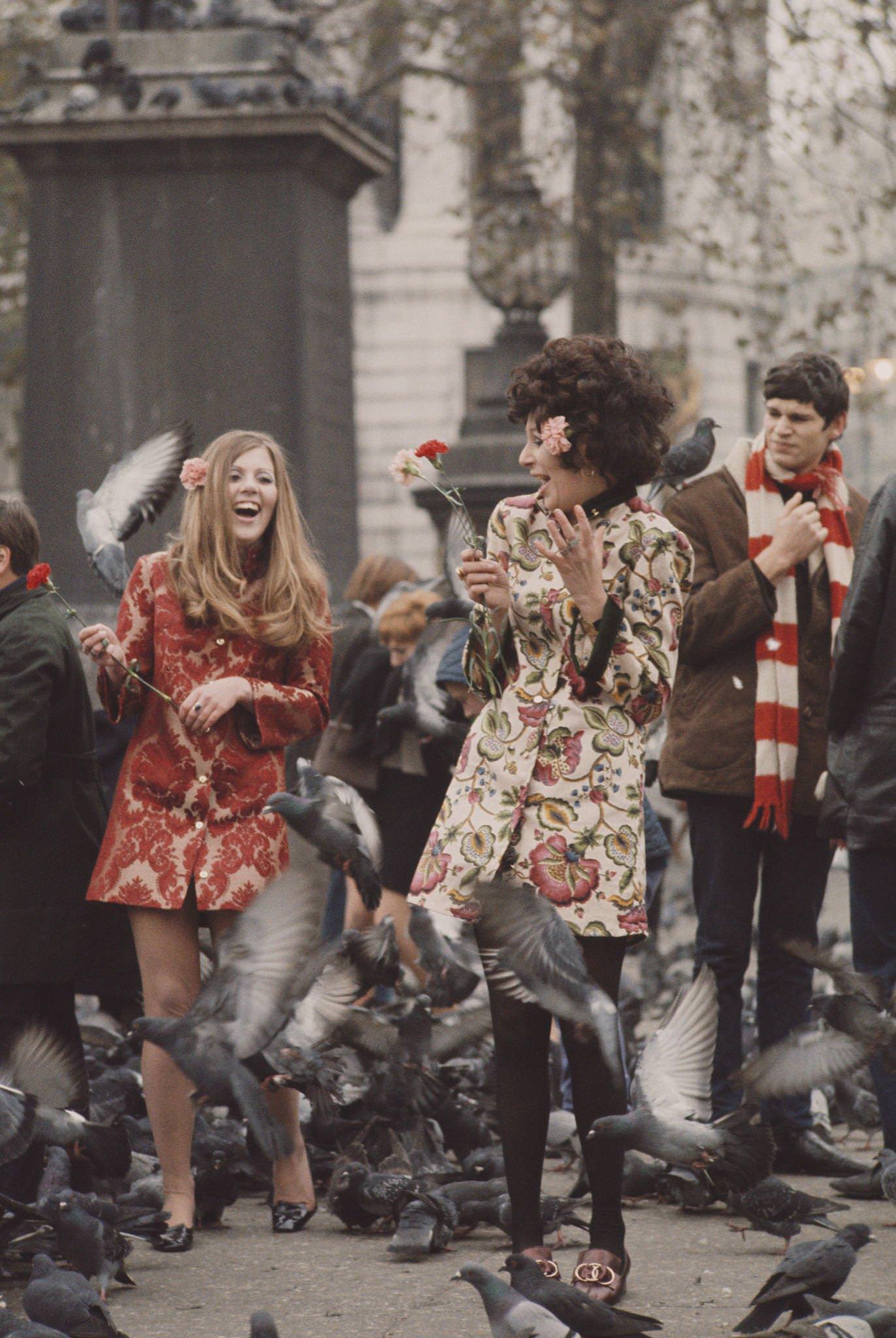 #10 Two young girls dressed in short floral brocade-print coats stand holding flowers as pigeons fly around them in Trafalgar Square, London in November 1967.