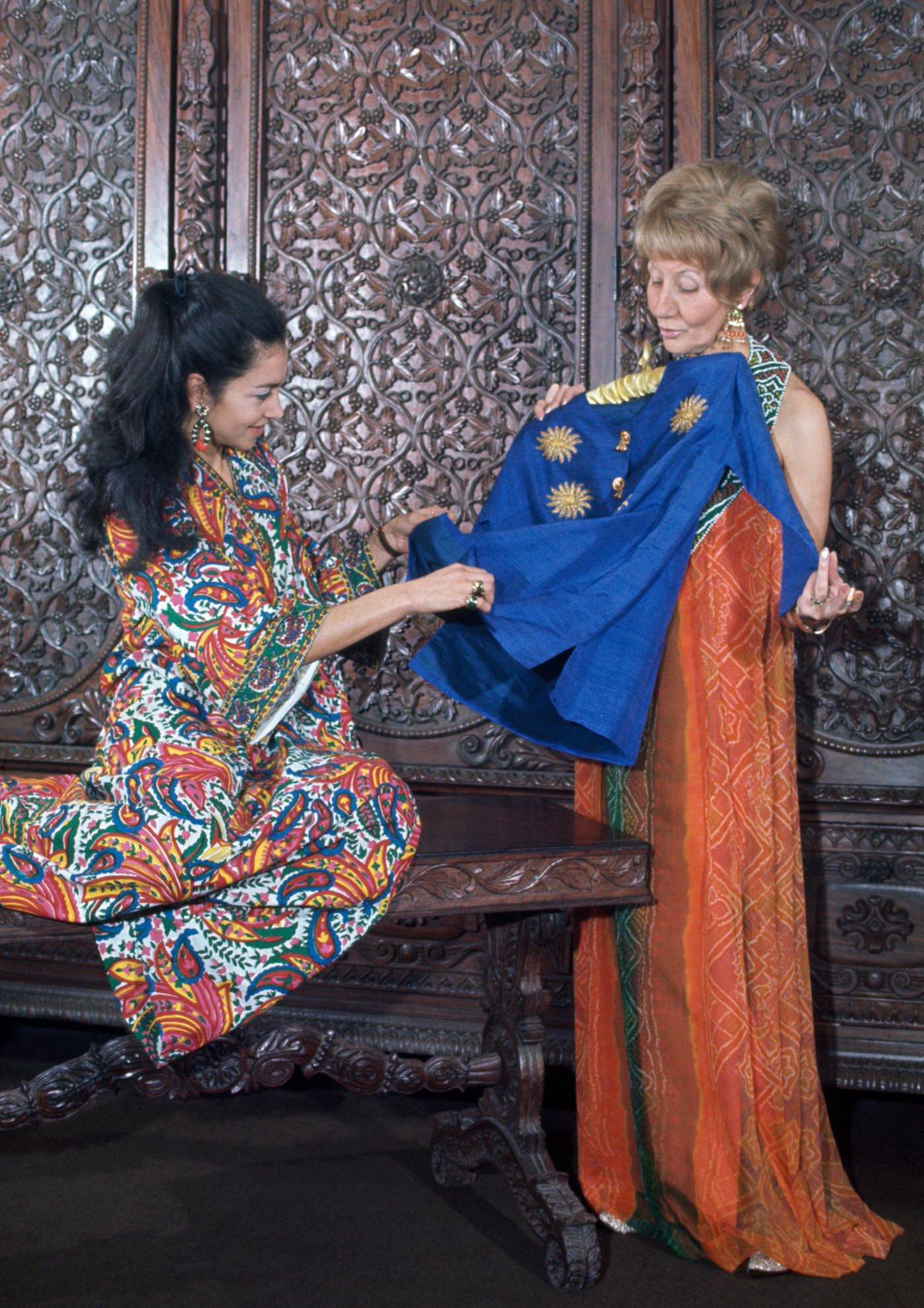 #11 Two women in a hippie fashion boutique, one wears a long orange halter neck dress, the other wears a kaftan dress in a vibrant floral print, London, 1966.