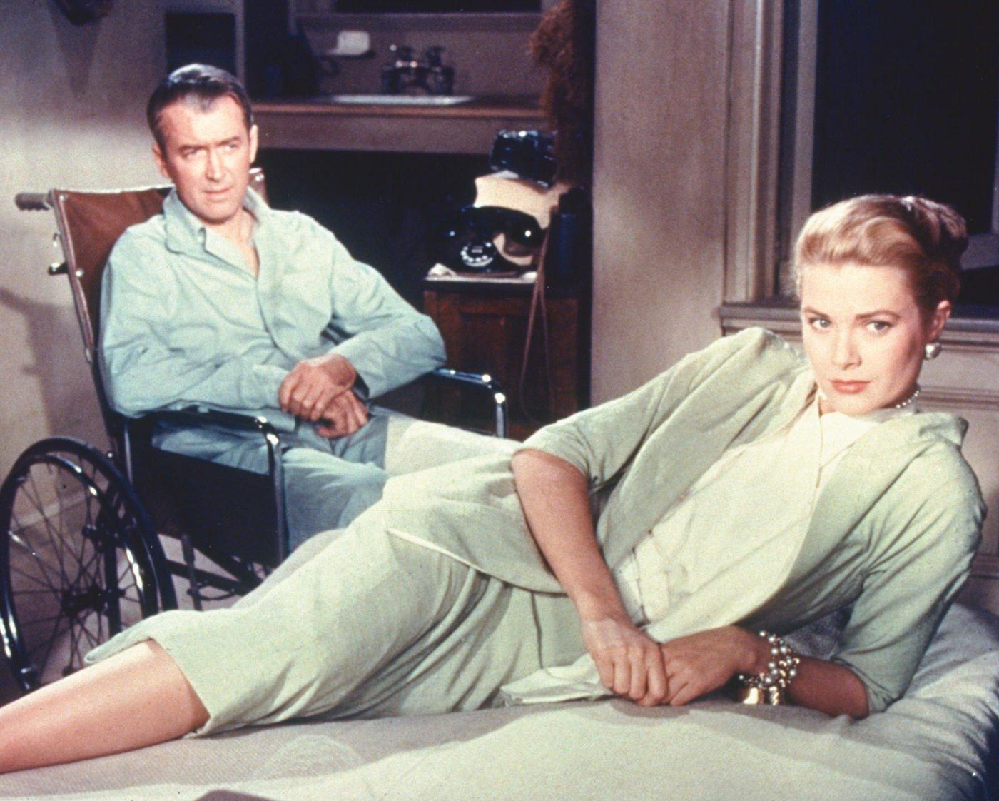 James Stewart wearing pyjamas as he sits in his wheelchair, while Grace Kelly lays on a bed in a publicity still issued for the film, ‘Rear Window’, 1954