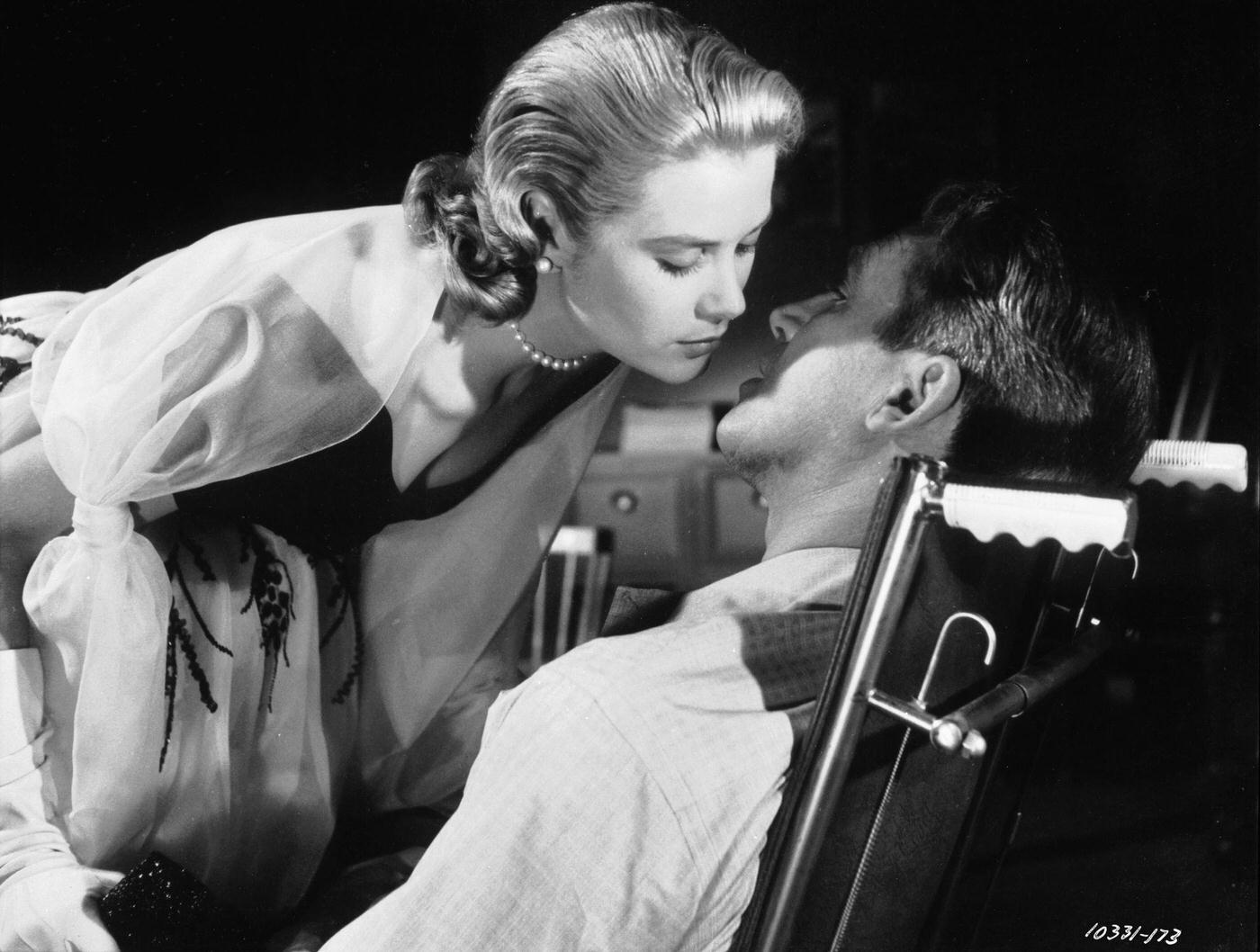 Grace Kelly leans over to kiss James Stewart in a scene from Hitchcock’s suspense mystery ‘Rear Window’. .