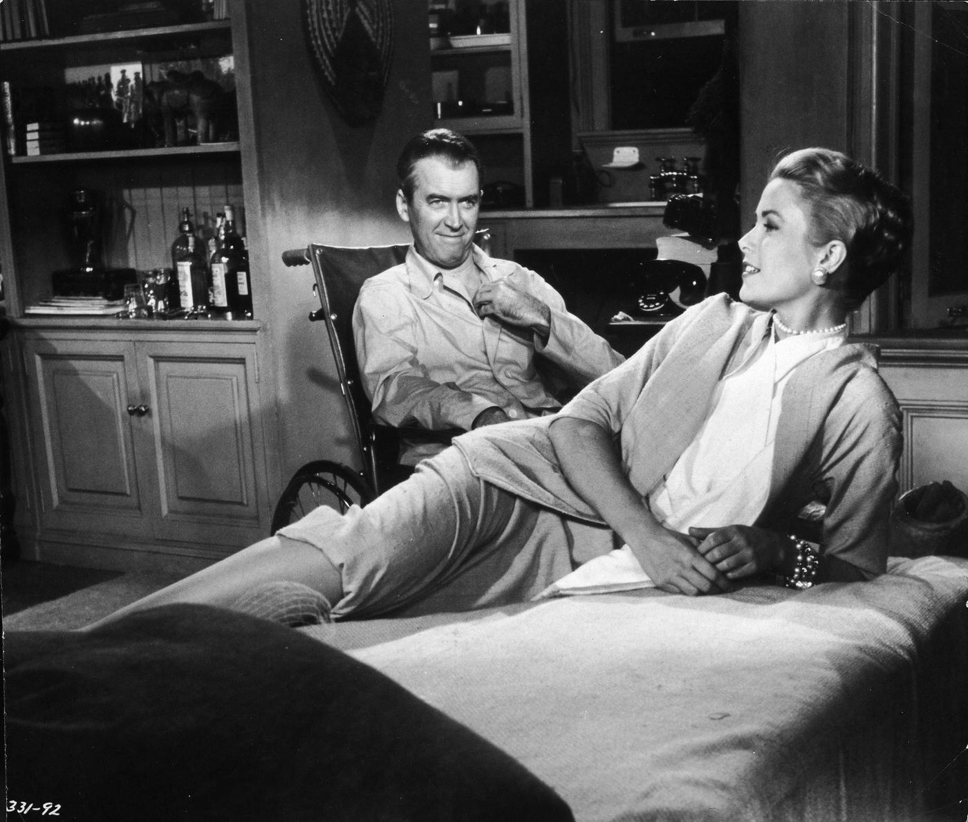 #58 Grace Kelly reclines on a bed while actor James Stewart smiles at her from a wheelchair in ‘Rear Window,’ 1954.