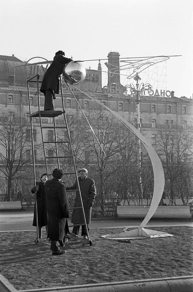 #57 Four men installing a model of Sputnik 1 on an abstract sculpture in a public garden.