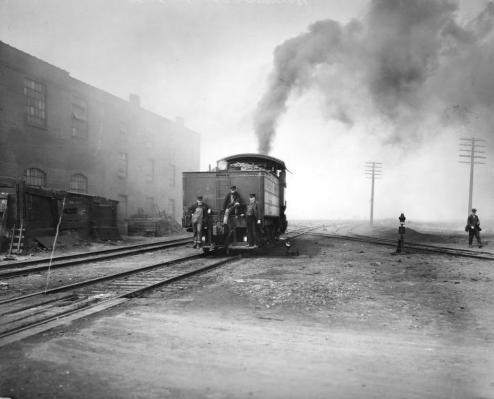 #12 Rear of a railway locomotive travelling away from the camera. Trainmen and an engineer are on the back of the Tender.