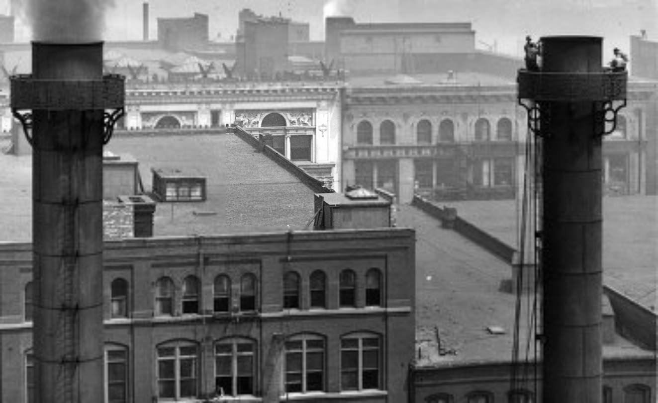 #15 A pair of smokestacks, one of which is being worked on by a group of men near the top of the stack, 1900. The upper stories and roofs of 901 and 911 Washington Avenue are visible in the background.