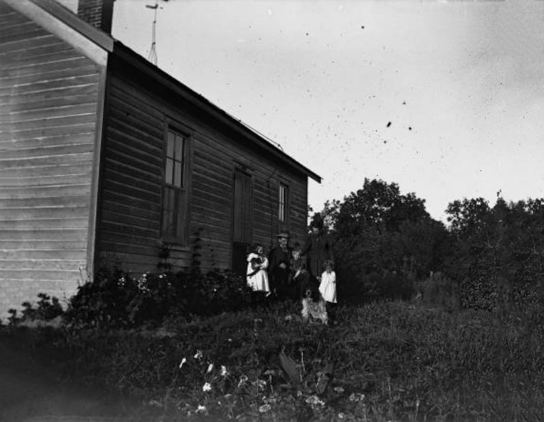 #199 Family poses in front of frame house, 1900