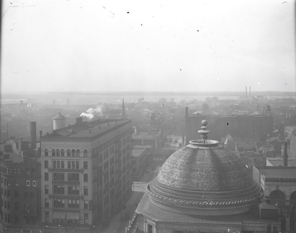 #3 An aerial view of Saint Louis. The view spans across rooftops with smokestacks in the distance, and the river in the background, 1900