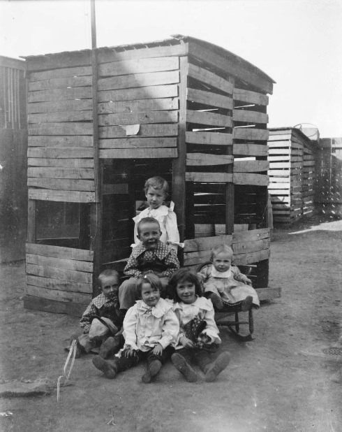 #228 Childrens sit for camera beside chicken coop, 1900
