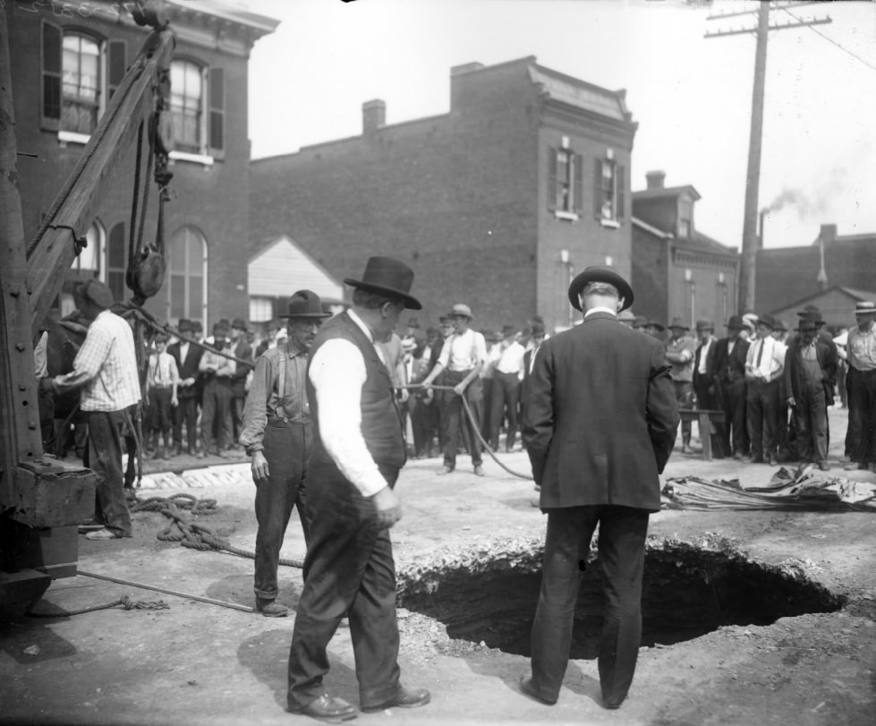 #39 People standing around a large hole in a city street, 1900