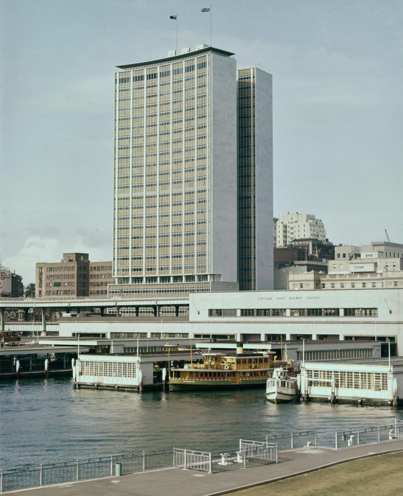 #95 A ferry docked at the Circular Quay Railway Station passenger terminal underneath the AMP Building office block in downtown Sydney, 1963