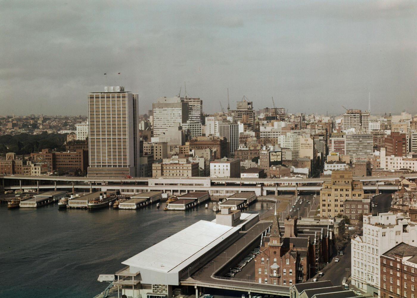 #97 Sydney Harbour Bridge of the Circular Quay wharves and Overseas Passenger Terminal overlooked by the recently completed AMP Building office block in downtown Sydney, 1963