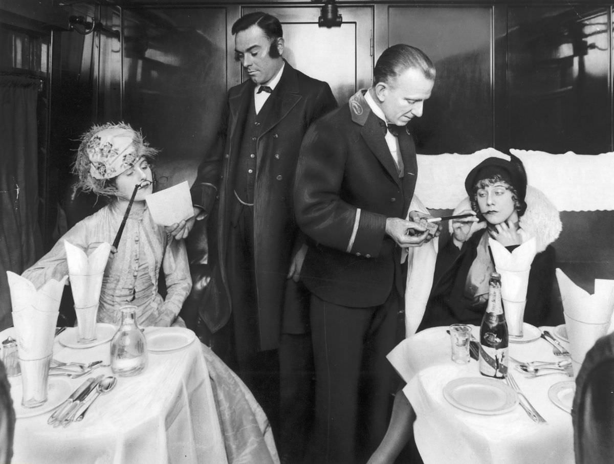 Two elegant ladies and waiters in a train dining car, Germany, 1929.