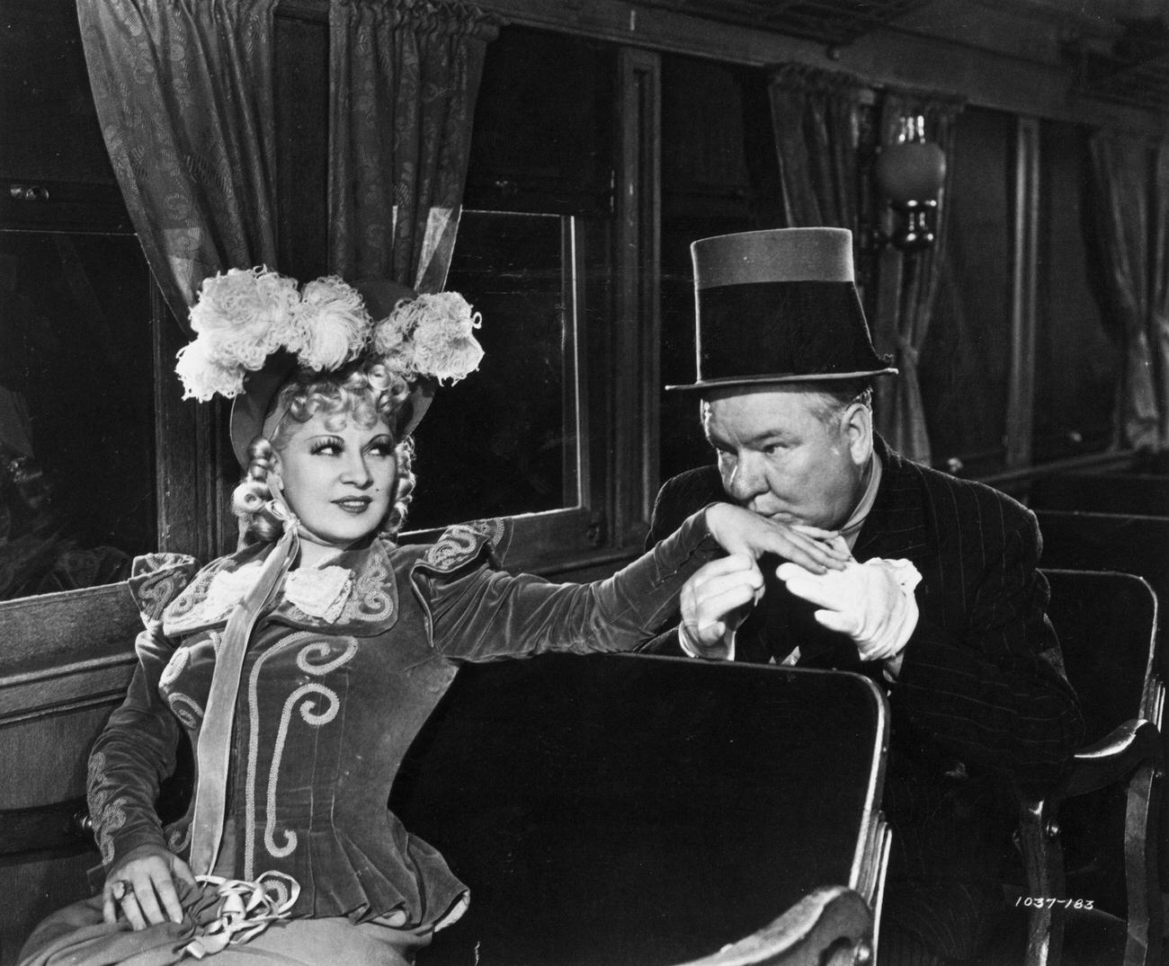 W C Fields kisses the hand of American writer, actor and comedian Mae West (1893 – 1980) while sitting aboard a train