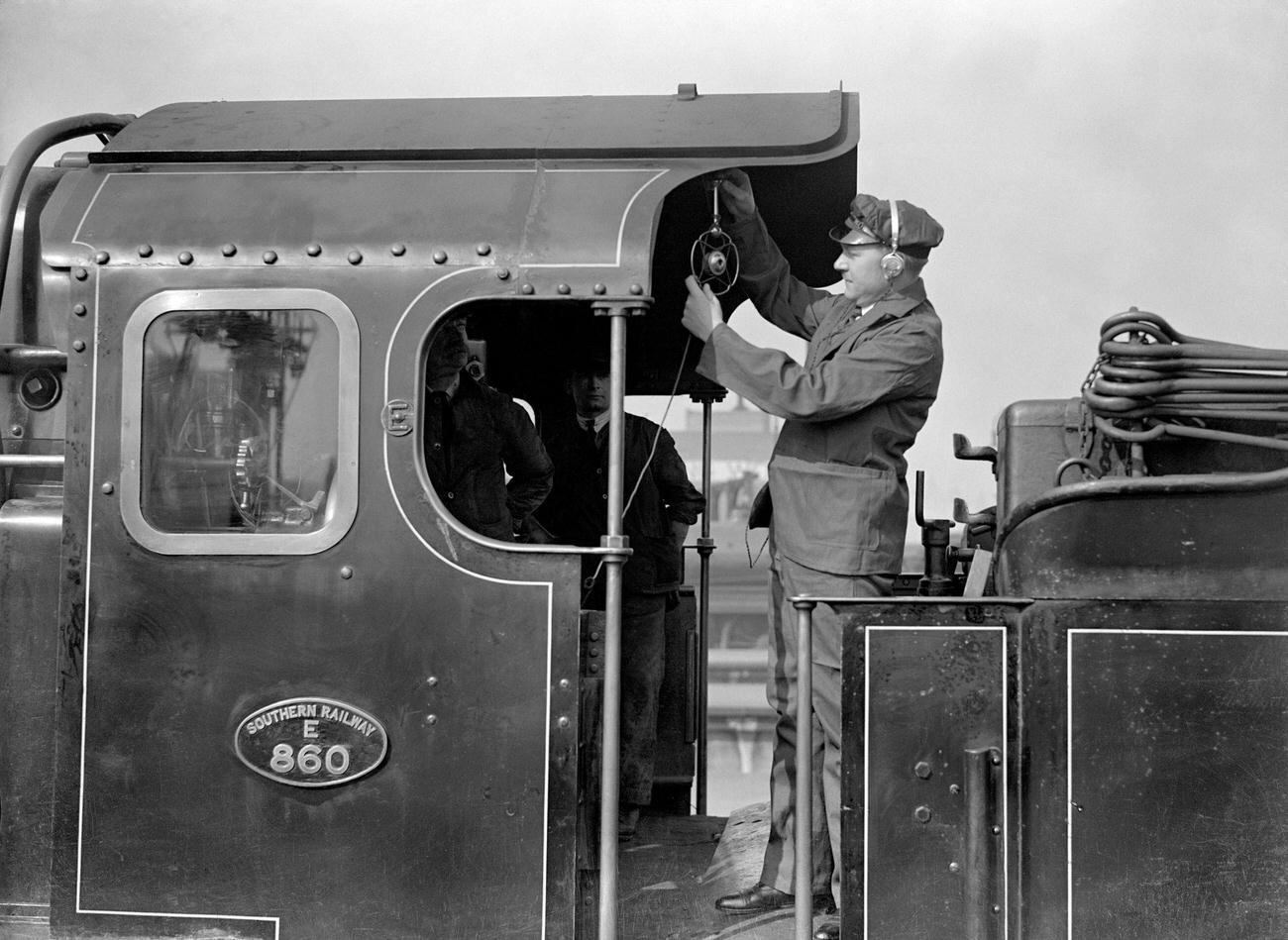 Reginald Foort traveling on the foot plate where he is seen adjusting the microphone, in an endeavour to secure local colour and time sound of which he will bemaking a gramaphone record of the popular “Choo Choo” train effects foxtrot.